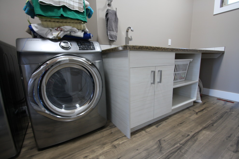 Example of a small minimalist single-wall medium tone wood floor dedicated laundry room design in Calgary with flat-panel cabinets, white cabinets, laminate countertops, beige walls and a side-by-side washer/dryer