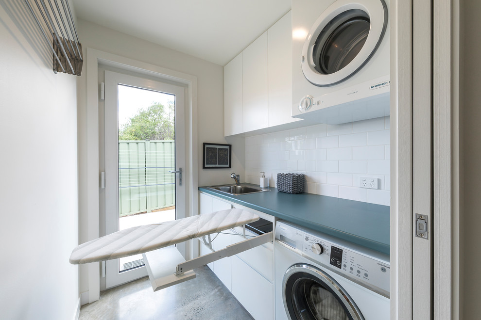 Zweizeilige, Kleine Moderne Waschküche mit Waschbecken, profilierten Schrankfronten, weißen Schränken, Laminat-Arbeitsplatte, weißer Wandfarbe, Betonboden, Waschmaschine und Trockner gestapelt, grauem Boden und blauer Arbeitsplatte in Canberra - Queanbeyan
