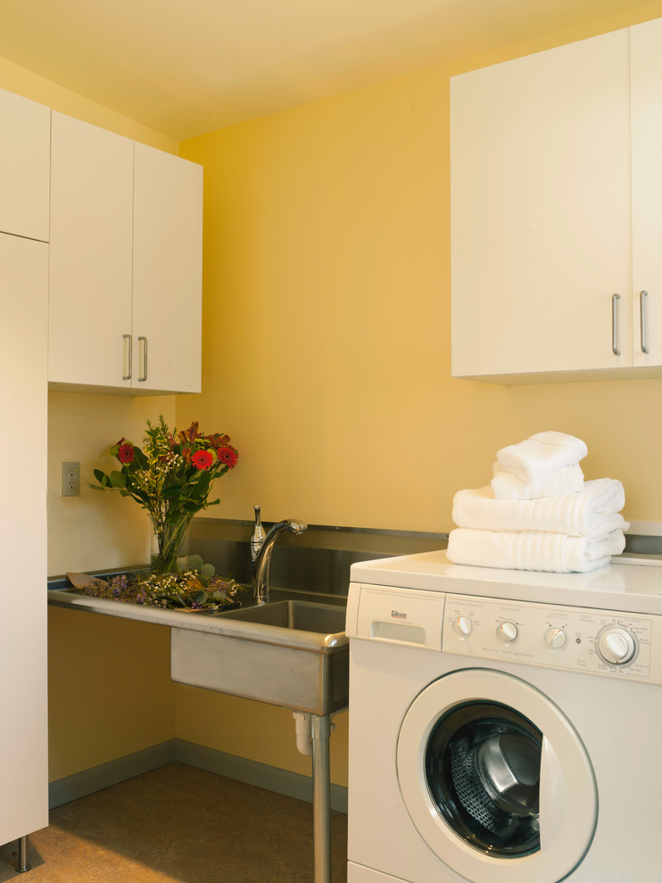 シアトルにある小さなミッドセンチュリースタイルのおしゃれな洗濯室 (ll型、アンダーカウンターシンク、フラットパネル扉のキャビネット、白いキャビネット、ステンレスカウンター、黄色い壁、セラミックタイルの床、左右配置の洗濯機・乾燥機) の写真