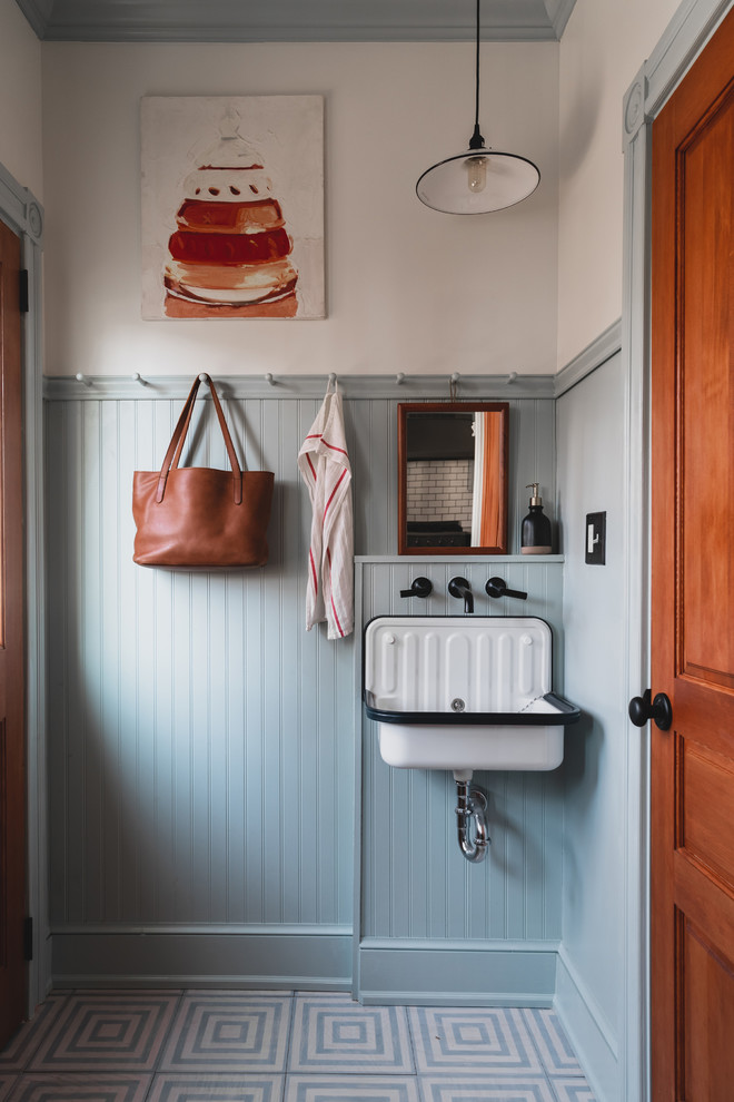 Modelo de lavadero multiusos tradicional pequeño con pila para lavar, armarios con paneles empotrados, puertas de armario azules, paredes azules, suelo de madera pintada, lavadora y secadora apiladas y suelo azul