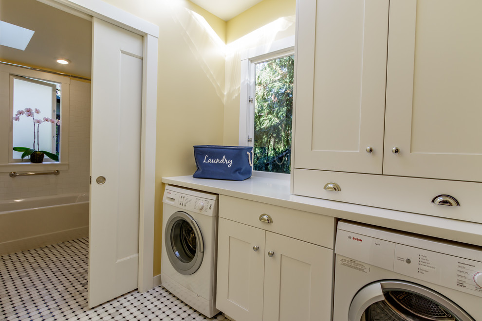 Exempel på en mellanstor amerikansk parallell tvättstuga enbart för tvätt, med skåp i shakerstil, vita skåp, bänkskiva i koppar, gula väggar, marmorgolv och en tvättmaskin och torktumlare bredvid varandra