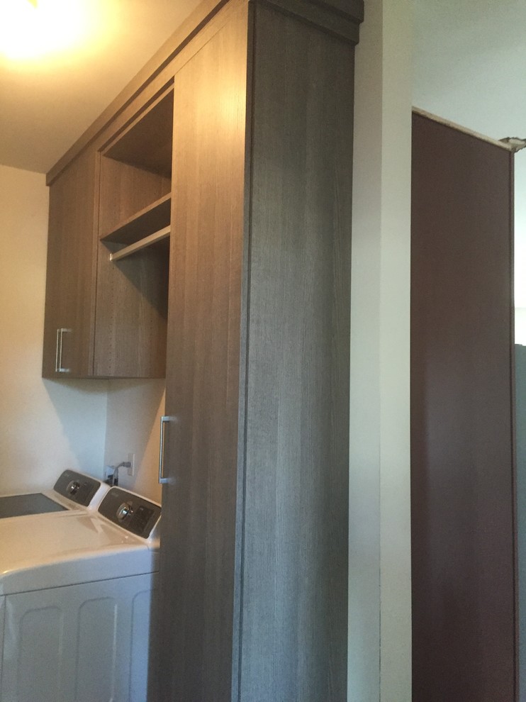 Photo of a small traditional single-wall utility room in New York with flat-panel cabinets, grey cabinets and a side by side washer and dryer.