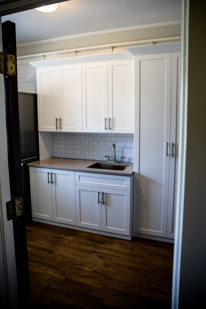 Example of a mid-sized cottage single-wall brown floor and dark wood floor utility room design in Atlanta with an undermount sink, shaker cabinets, white cabinets, granite countertops, gray walls, a stacked washer/dryer and gray countertops