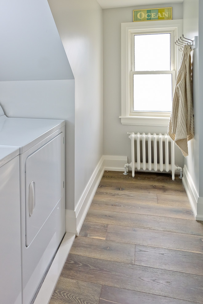 Immagine di una sala lavanderia classica di medie dimensioni con pareti bianche, pavimento in legno massello medio e lavatrice e asciugatrice affiancate