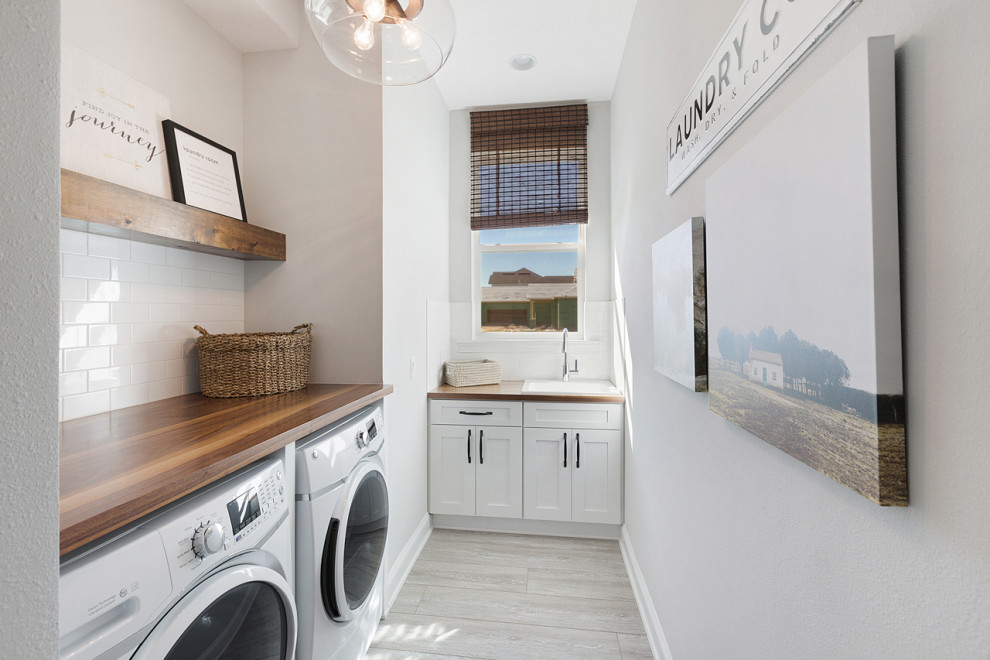 Dedicated laundry room - mid-sized country l-shaped vinyl floor and gray floor dedicated laundry room idea in Jacksonville with a drop-in sink, shaker cabinets, white cabinets, wood countertops, white walls, an integrated washer/dryer and brown countertops