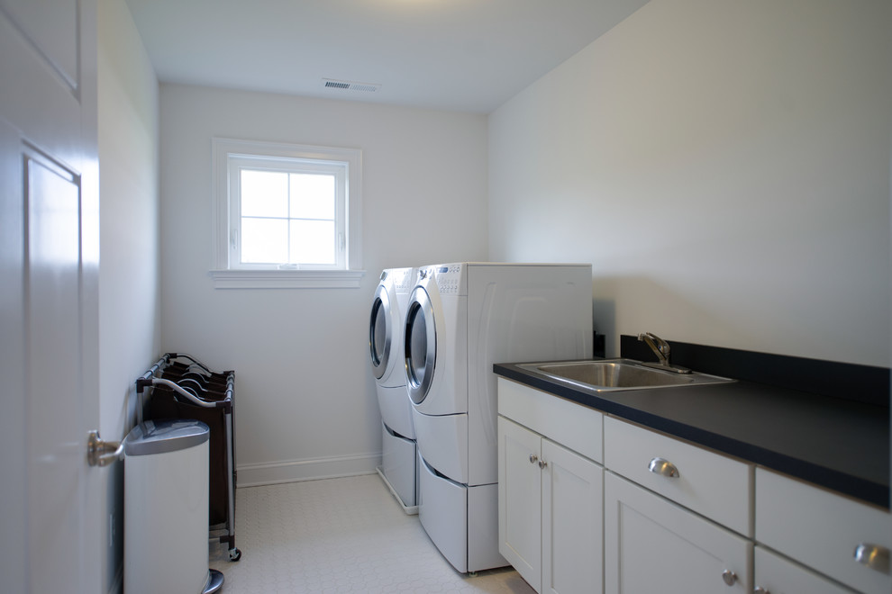 Ejemplo de cuarto de lavado de galera clásico con fregadero encastrado, puertas de armario blancas, paredes blancas, lavadora y secadora juntas y encimeras negras