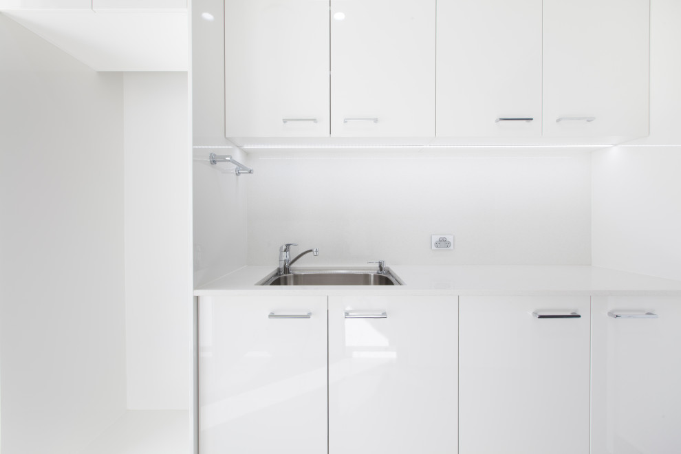 Exempel på en mellanstor modern vita parallell vitt tvättstuga enbart för tvätt, med en undermonterad diskho, släta luckor, vita skåp, bänkskiva i kvarts, vitt stänkskydd, vita väggar, klinkergolv i porslin, en tvättpelare och grått golv