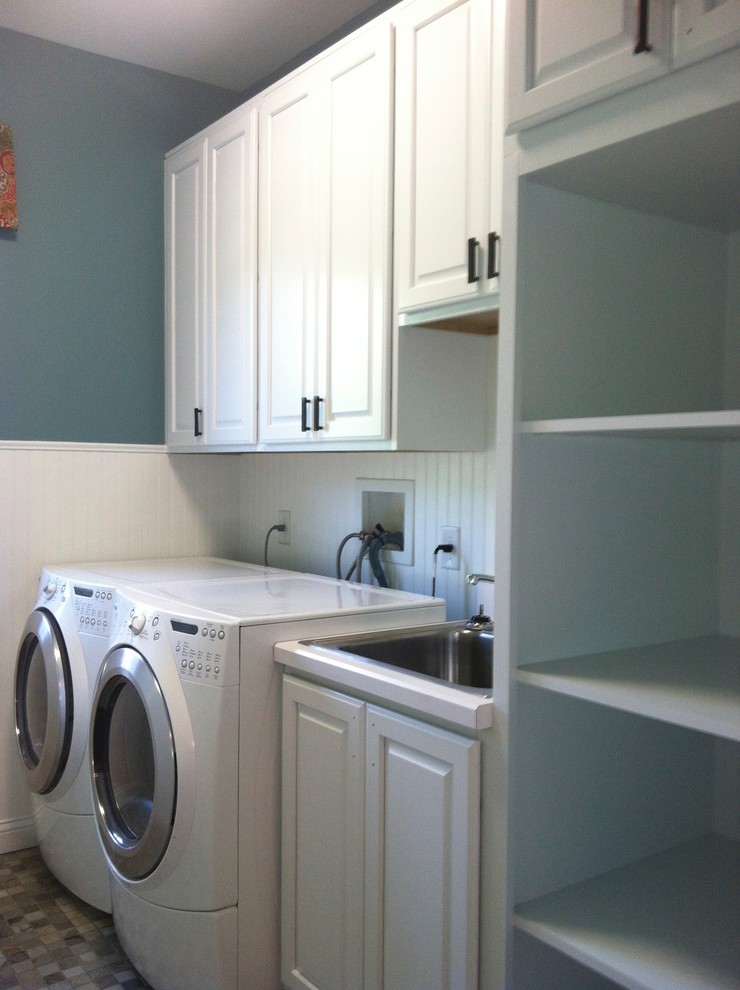 Foto på en vintage tvättstuga, med en nedsänkt diskho, luckor med upphöjd panel, vita skåp, blå väggar och en tvättmaskin och torktumlare bredvid varandra