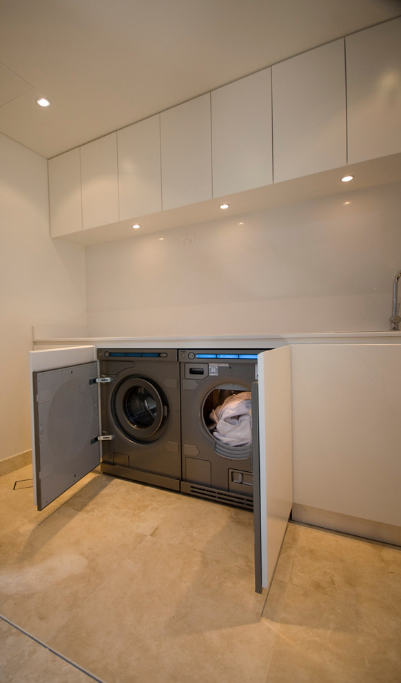 Idéer för att renovera en funkis linjär tvättstuga enbart för tvätt, med en undermonterad diskho, vita skåp, bänkskiva i kvarts, vita väggar och tvättmaskin och torktumlare byggt in i ett skåp