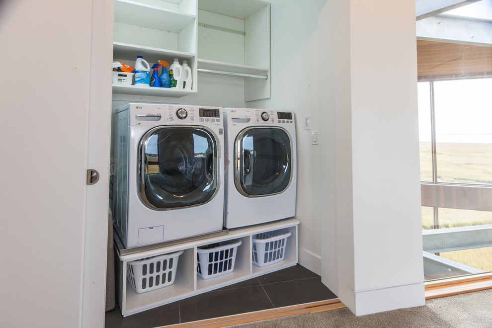 Imagen de armario lavadero lineal moderno de tamaño medio con armarios abiertos, paredes blancas, suelo de baldosas de porcelana y lavadora y secadora juntas