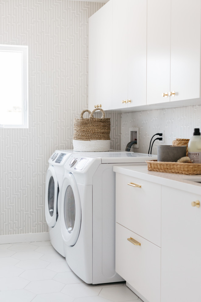Lantlig inredning av en mellanstor vita linjär vitt tvättstuga enbart för tvätt, med en undermonterad diskho, släta luckor, vita skåp, grå väggar, klinkergolv i porslin, en tvättmaskin och torktumlare bredvid varandra och vitt golv