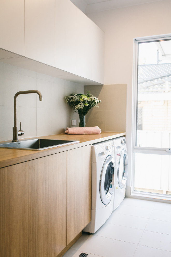 Photo of a modern separated utility room in Perth with a single-bowl sink, light wood cabinets, wood worktops, grey walls, a side by side washer and dryer, ceramic flooring and white floors.