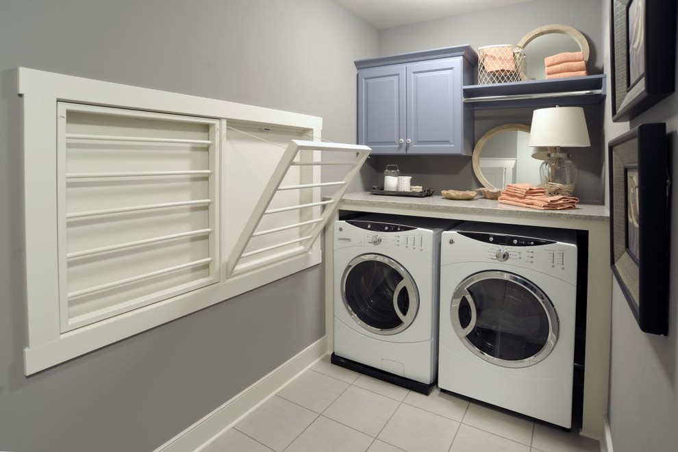 Imagen de cuarto de lavado en L clásico con paredes grises, armarios con paneles con relieve, puertas de armario azules, lavadora y secadora juntas y suelo gris