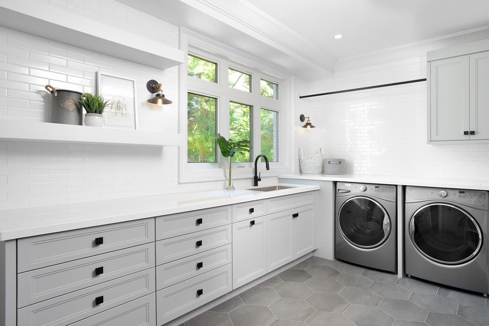 Idéer för att renovera en vintage vita l-formad vitt tvättstuga enbart för tvätt, med en undermonterad diskho, luckor med infälld panel, grå skåp, vita väggar, en tvättmaskin och torktumlare bredvid varandra och grått golv