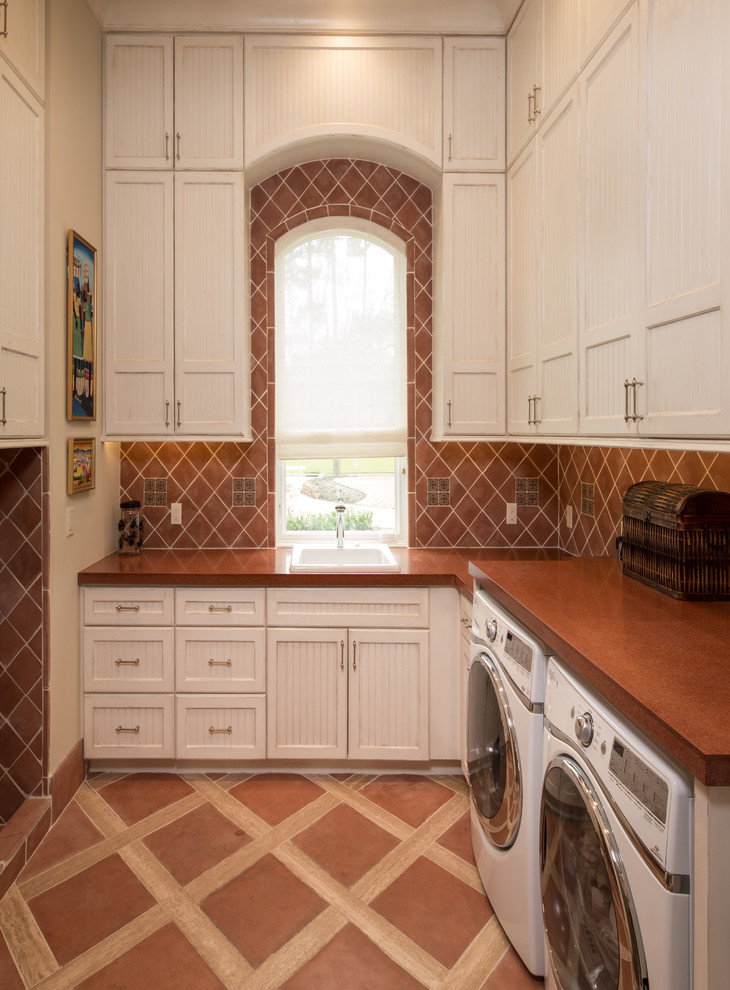 Photo of a mediterranean u-shaped separated utility room in Houston with a built-in sink, recessed-panel cabinets, white cabinets, a side by side washer and dryer, ceramic flooring and brown worktops.