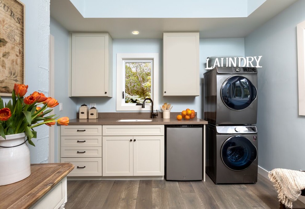 Photo of a medium sized nautical single-wall utility room in Santa Barbara with quartz worktops, blue walls, medium hardwood flooring, a stacked washer and dryer, brown floors, brown worktops, a submerged sink, shaker cabinets and beige cabinets.