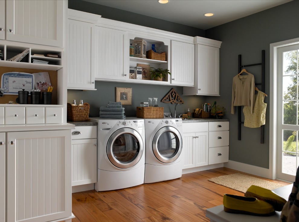 Idéer för en stor klassisk linjär tvättstuga enbart för tvätt, med en nedsänkt diskho, luckor med infälld panel, vita skåp, granitbänkskiva, grå väggar, mörkt trägolv, en tvättmaskin och torktumlare bredvid varandra och brunt golv