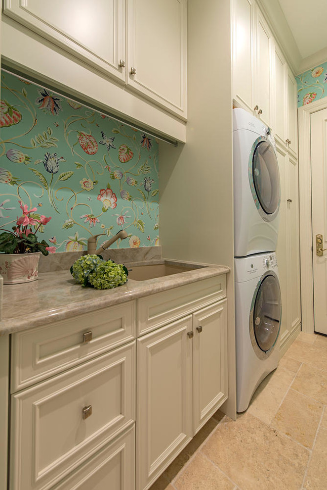 マイアミにある高級な広いトランジショナルスタイルのおしゃれな洗濯室 (アンダーカウンターシンク、I型、マルチカラーの壁、トラバーチンの床、上下配置の洗濯機・乾燥機、落し込みパネル扉のキャビネット、ベージュのキャビネット) の写真