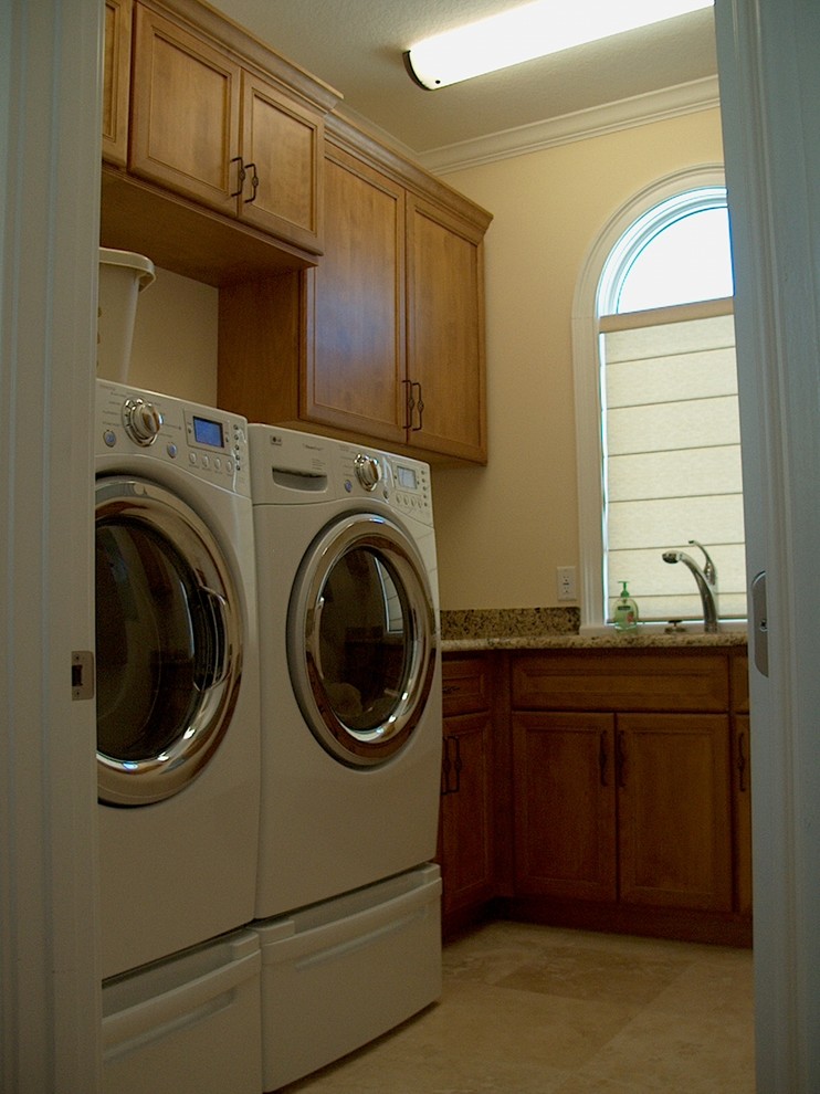 Foto på en medelhavsstil beige tvättstuga, med luckor med infälld panel, skåp i mellenmörkt trä, granitbänkskiva, gula väggar, en tvättmaskin och torktumlare bredvid varandra och beiget golv