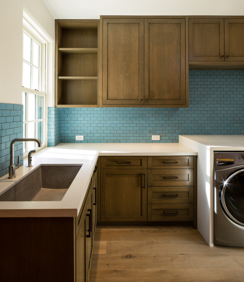 Idéer för en mellanstor klassisk l-formad tvättstuga enbart för tvätt, med en undermonterad diskho, luckor med profilerade fronter, vita skåp, blå väggar, mellanmörkt trägolv och en tvättmaskin och torktumlare bredvid varandra