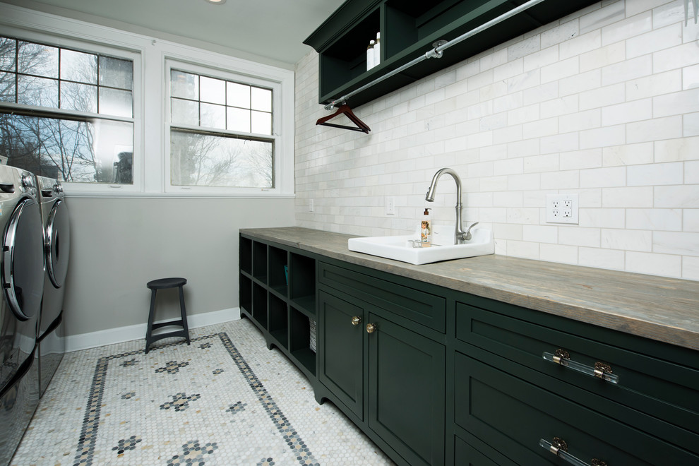 Inredning av en klassisk mellanstor parallell tvättstuga enbart för tvätt, med skåp i shakerstil, grå skåp, marmorgolv, vitt golv, en nedsänkt diskho, träbänkskiva, en tvättmaskin och torktumlare bredvid varandra och grå väggar