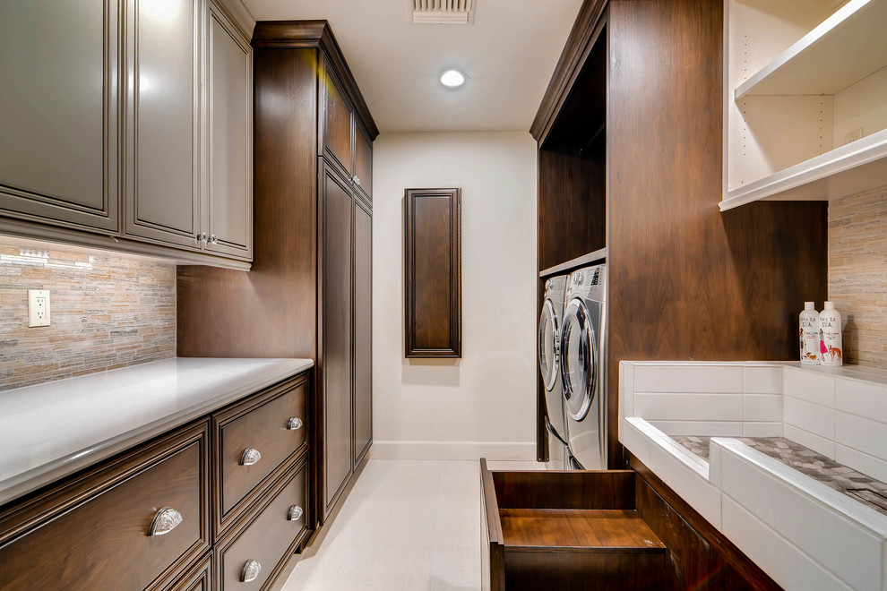 Photo of a large bohemian galley utility room in Phoenix with an utility sink, raised-panel cabinets, engineered stone countertops, white walls, porcelain flooring, a side by side washer and dryer, beige floors and dark wood cabinets.