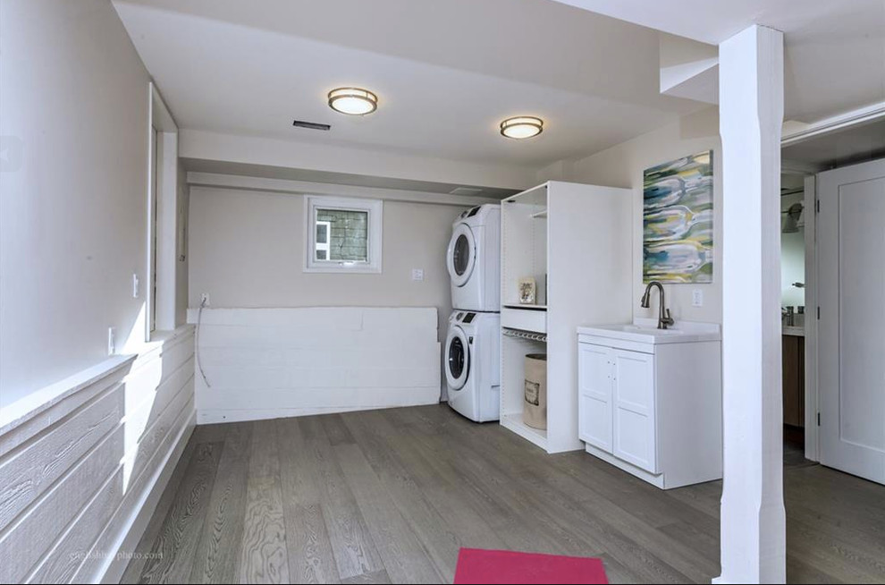 Large contemporary single-wall utility room in Vancouver with a submerged sink, shaker cabinets, white cabinets, quartz worktops, beige walls, light hardwood flooring, a stacked washer and dryer, brown floors and white worktops.