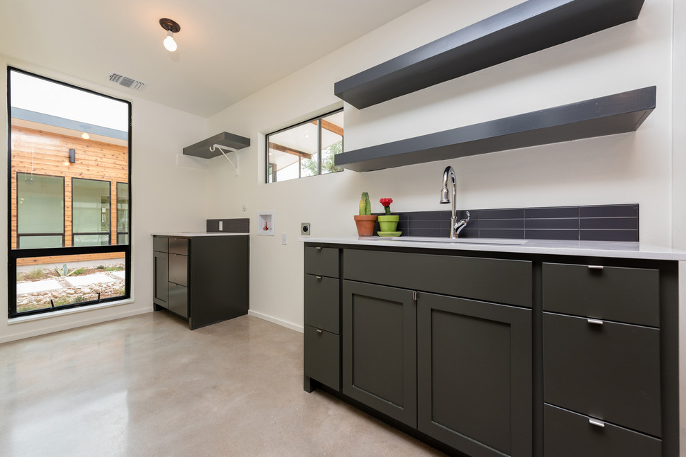 Example of a large 1960s l-shaped concrete floor utility room design in Austin with an undermount sink, shaker cabinets, black cabinets, quartz countertops, white walls and a side-by-side washer/dryer