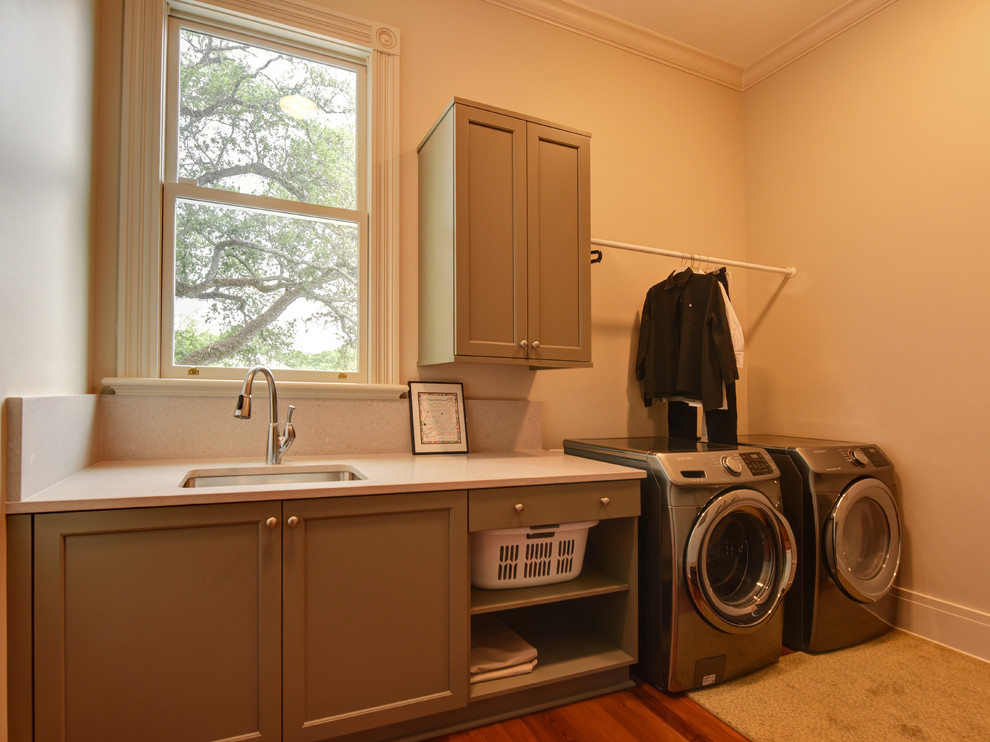 Medium sized traditional single-wall utility room in New Orleans with brown floors, a submerged sink, shaker cabinets, grey cabinets, beige walls, medium hardwood flooring and a side by side washer and dryer.