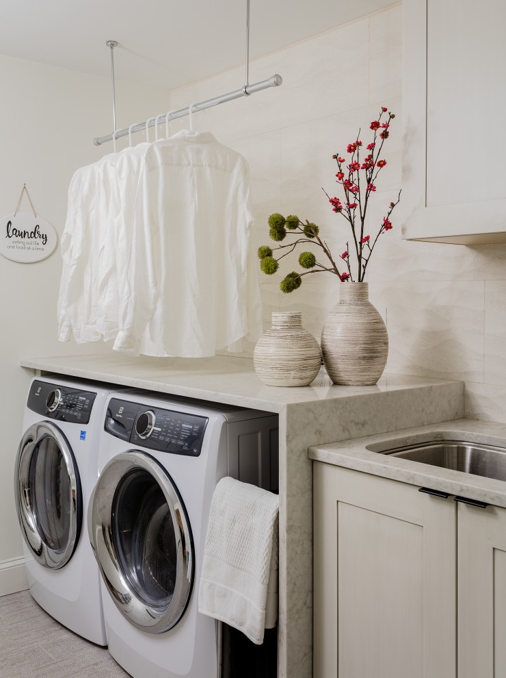Inredning av en modern grå linjär grått tvättstuga, med en undermonterad diskho, skåp i shakerstil, grå skåp, en tvättmaskin och torktumlare bredvid varandra och grått golv