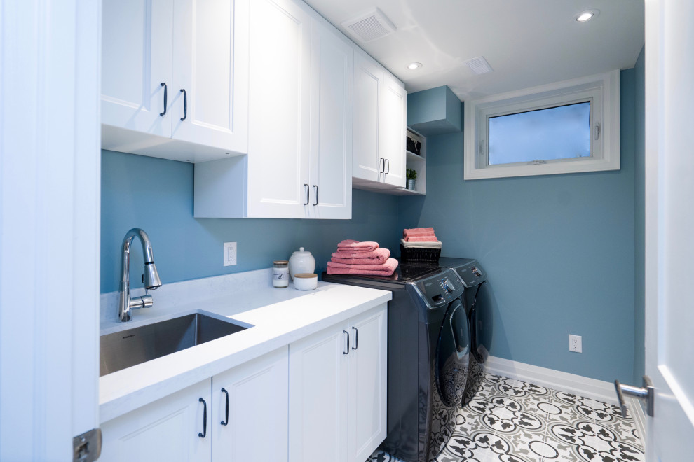 Exempel på en klassisk vita linjär vitt tvättstuga enbart för tvätt, med en undermonterad diskho, skåp i shakerstil, vita skåp, bänkskiva i kvarts, vitt stänkskydd, blå väggar, klinkergolv i porslin, en tvättmaskin och torktumlare bredvid varandra och flerfärgat golv