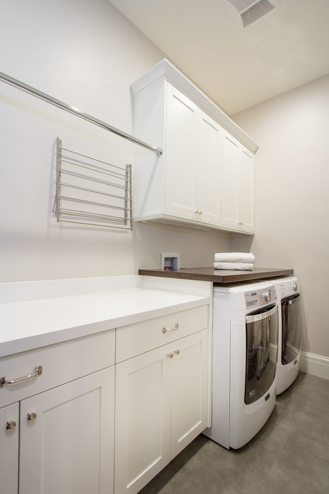 Klassisk inredning av en mellanstor vita linjär vitt tvättstuga enbart för tvätt, med skåp i shakerstil, vita skåp, bänkskiva i kvarts, grå väggar, betonggolv, en tvättmaskin och torktumlare bredvid varandra och grått golv