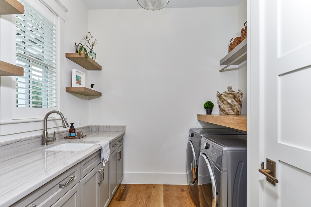 Inspiration for a mid-sized transitional galley brown floor and medium tone wood floor dedicated laundry room remodel in Other with an undermount sink, recessed-panel cabinets, gray cabinets, granite countertops, white walls, a side-by-side washer/dryer and white countertops