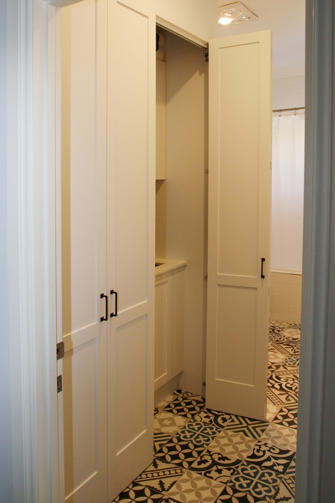 Example of a mid-sized cottage chic single-wall ceramic tile and multicolored floor utility room design in Sydney with shaker cabinets, white cabinets, solid surface countertops, white walls, an undermount sink, an integrated washer/dryer and white countertops