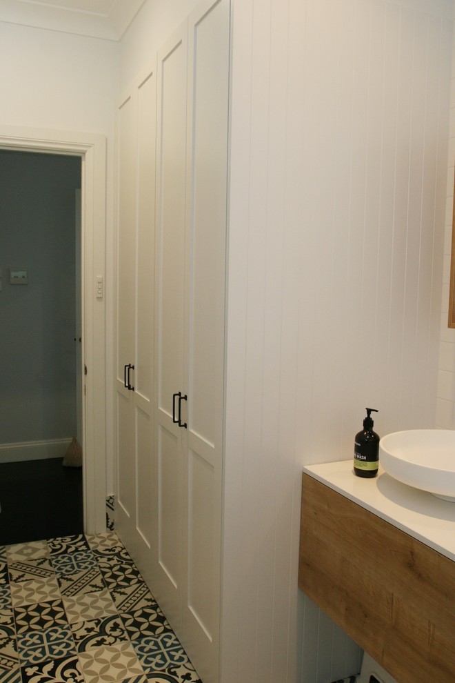 Example of a mid-sized cottage chic single-wall ceramic tile and multicolored floor utility room design in Sydney with an undermount sink, shaker cabinets, white cabinets, solid surface countertops, white walls, an integrated washer/dryer and white countertops