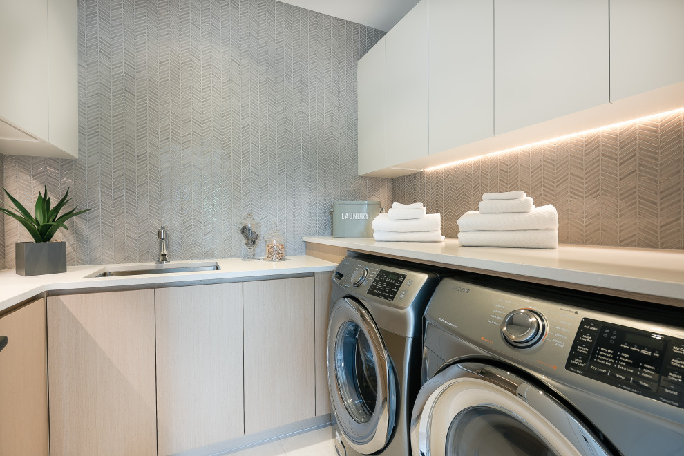 Idéer för att renovera en stor funkis vita parallell vitt tvättstuga enbart för tvätt, med en undermonterad diskho, släta luckor, skåp i ljust trä, bänkskiva i kvarts, grått stänkskydd, stänkskydd i mosaik, grå väggar, klinkergolv i porslin, en tvättmaskin och torktumlare bredvid varandra och vitt golv