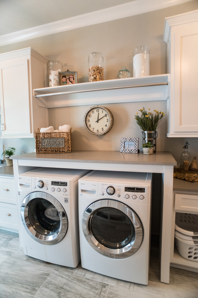 Foto på en stor vintage tvättstuga enbart för tvätt, med en undermonterad diskho, vita skåp, bänkskiva i kvarts, grå väggar, klinkergolv i porslin, en tvättmaskin och torktumlare bredvid varandra och luckor med infälld panel