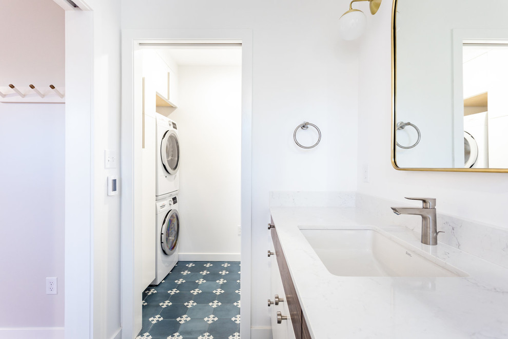 Mid-sized trendy galley blue floor dedicated laundry room photo in Portland with flat-panel cabinets, white cabinets, quartz countertops, white walls, a stacked washer/dryer and white countertops