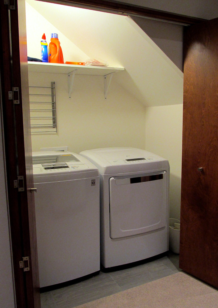 Exempel på en liten modern linjär liten tvättstuga, med vita väggar, klinkergolv i porslin och en tvättmaskin och torktumlare bredvid varandra