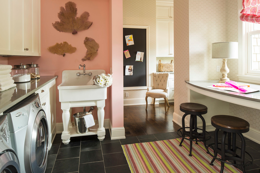 ミネアポリスにあるトランジショナルスタイルのおしゃれなランドリールーム (白いキャビネット、黒い床、スロップシンク、シェーカースタイル扉のキャビネット、ピンクの壁、左右配置の洗濯機・乾燥機) の写真