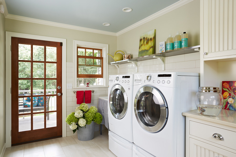 Lantlig inredning av en mellanstor linjär tvättstuga, med en allbänk, en tvättmaskin och torktumlare bredvid varandra, luckor med infälld panel, vita skåp, bänkskiva i kvarts och klinkergolv i porslin
