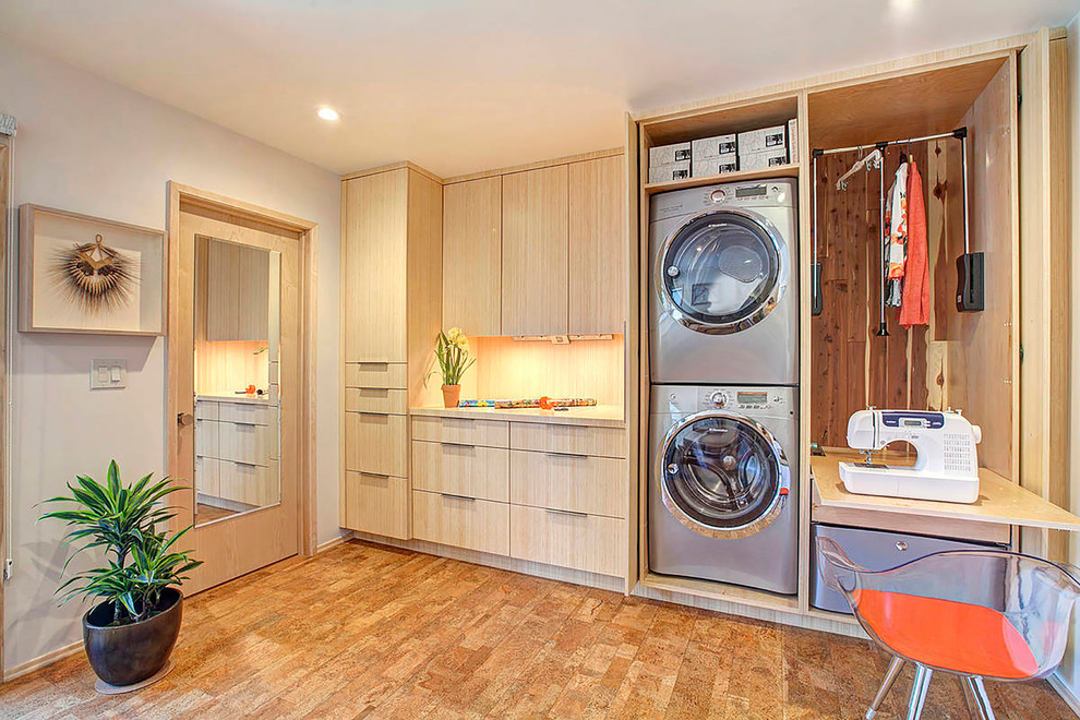 Ejemplo de lavadero multiusos y lineal actual con armarios con paneles lisos, puertas de armario de madera clara, paredes grises, lavadora y secadora escondidas y suelo de corcho