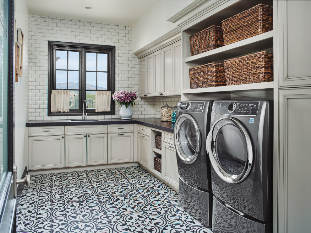 Idéer för medelhavsstil l-formade svart tvättstugor enbart för tvätt, med en undermonterad diskho, luckor med infälld panel, grå skåp, vitt stänkskydd, stänkskydd i tunnelbanekakel, vita väggar, en tvättmaskin och torktumlare bredvid varandra och flerfärgat golv