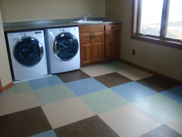 Klassisk inredning av en stor tvättstuga enbart för tvätt, med en nedsänkt diskho, skåp i shakerstil, skåp i mellenmörkt trä, beige väggar, vinylgolv, en tvättmaskin och torktumlare bredvid varandra och flerfärgat golv
