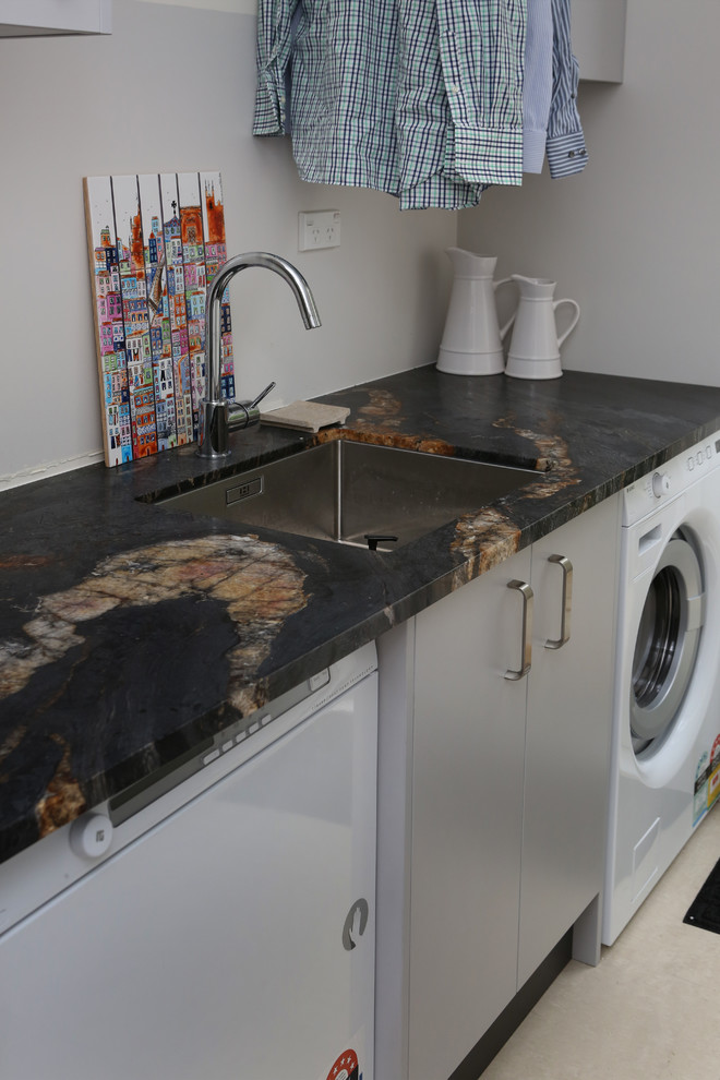 Photo of a small contemporary single-wall separated utility room in Auckland with a submerged sink, flat-panel cabinets, grey cabinets, granite worktops, grey walls, porcelain flooring, a side by side washer and dryer and white floors.