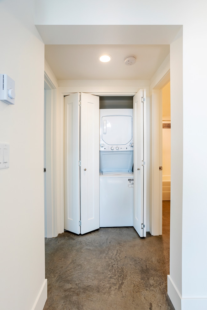 Foto de armario lavadero lineal contemporáneo pequeño con paredes blancas, suelo de cemento, lavadora y secadora apiladas y suelo gris