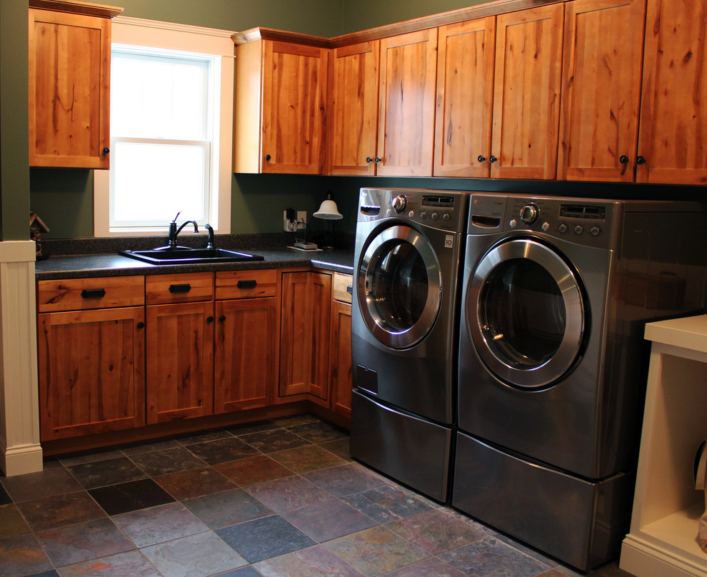Idéer för en stor amerikansk l-formad tvättstuga enbart för tvätt, med en nedsänkt diskho, luckor med infälld panel, skåp i mellenmörkt trä, bänkskiva i koppar, gröna väggar, skiffergolv och en tvättmaskin och torktumlare bredvid varandra