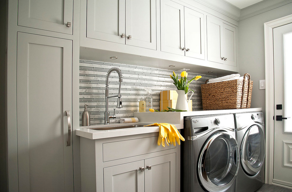 Inspiration for a transitional single-wall porcelain tile utility room remodel in Toronto with shaker cabinets, gray cabinets, solid surface countertops, gray walls, a side-by-side washer/dryer, white countertops and a drop-in sink