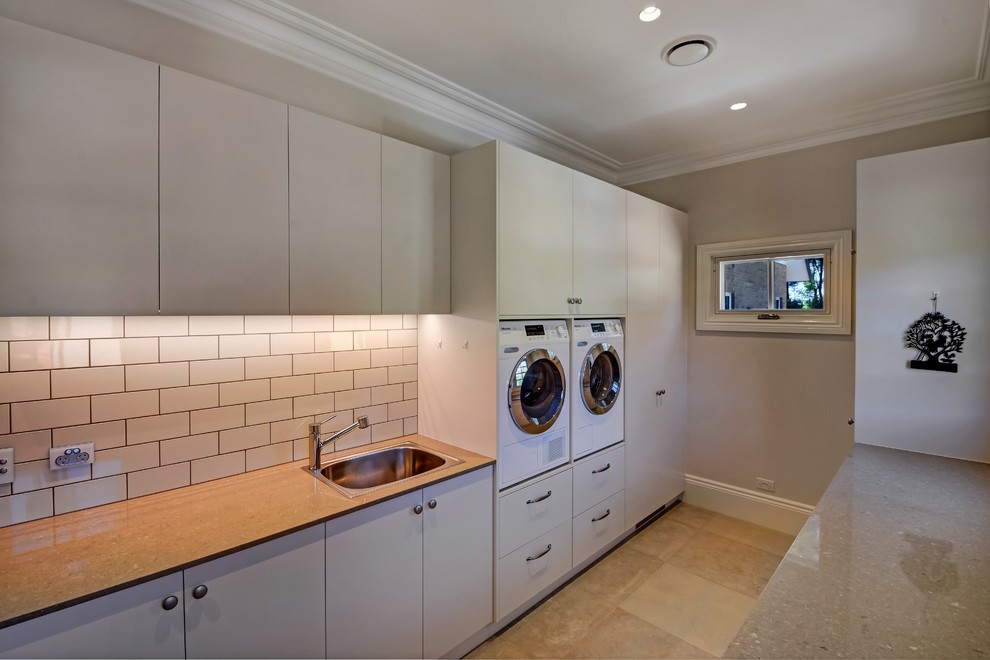 Large rural galley utility room in Other with a built-in sink, flat-panel cabinets, grey cabinets, composite countertops, beige walls, ceramic flooring, a side by side washer and dryer and brown floors.