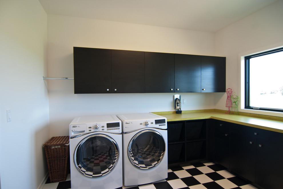 Modelo de lavadero moderno con armarios con paneles lisos, puertas de armario negras, paredes blancas y lavadora y secadora juntas
